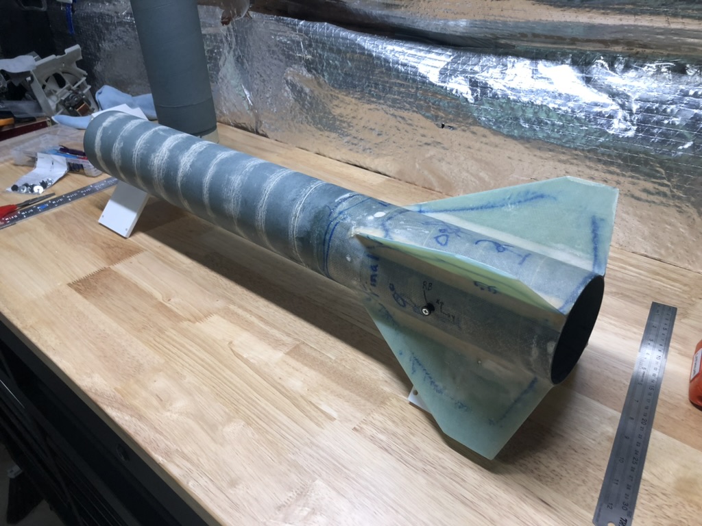 A rocket airframe with tip-to-tip fiberglass layup and custom surface mounted G10 fiberglass fins on a workbench